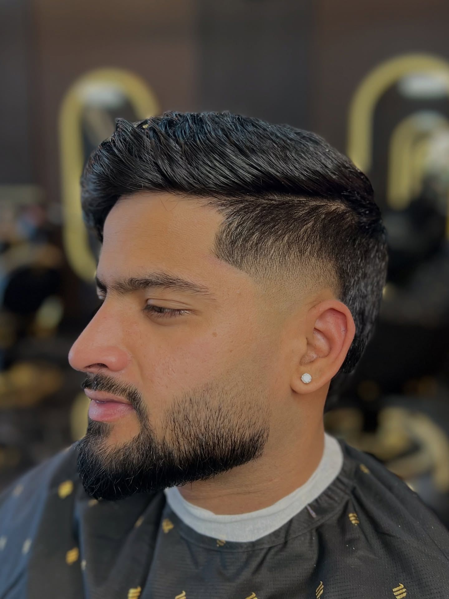 A client with slicked-back hair, a burst fade and a full shaped beard