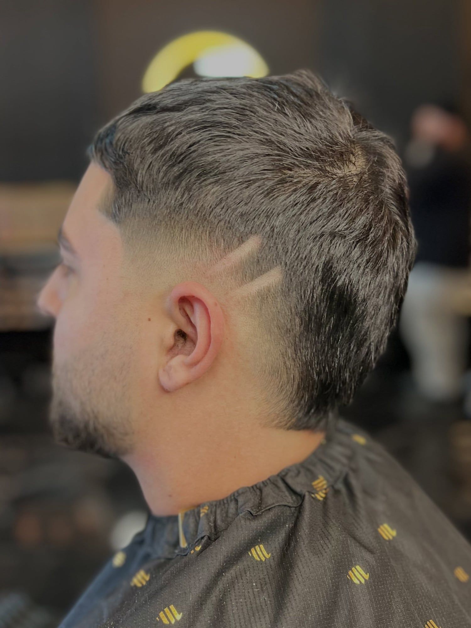 A client in profile with a low taper fade and two razor lines cut in above the ear