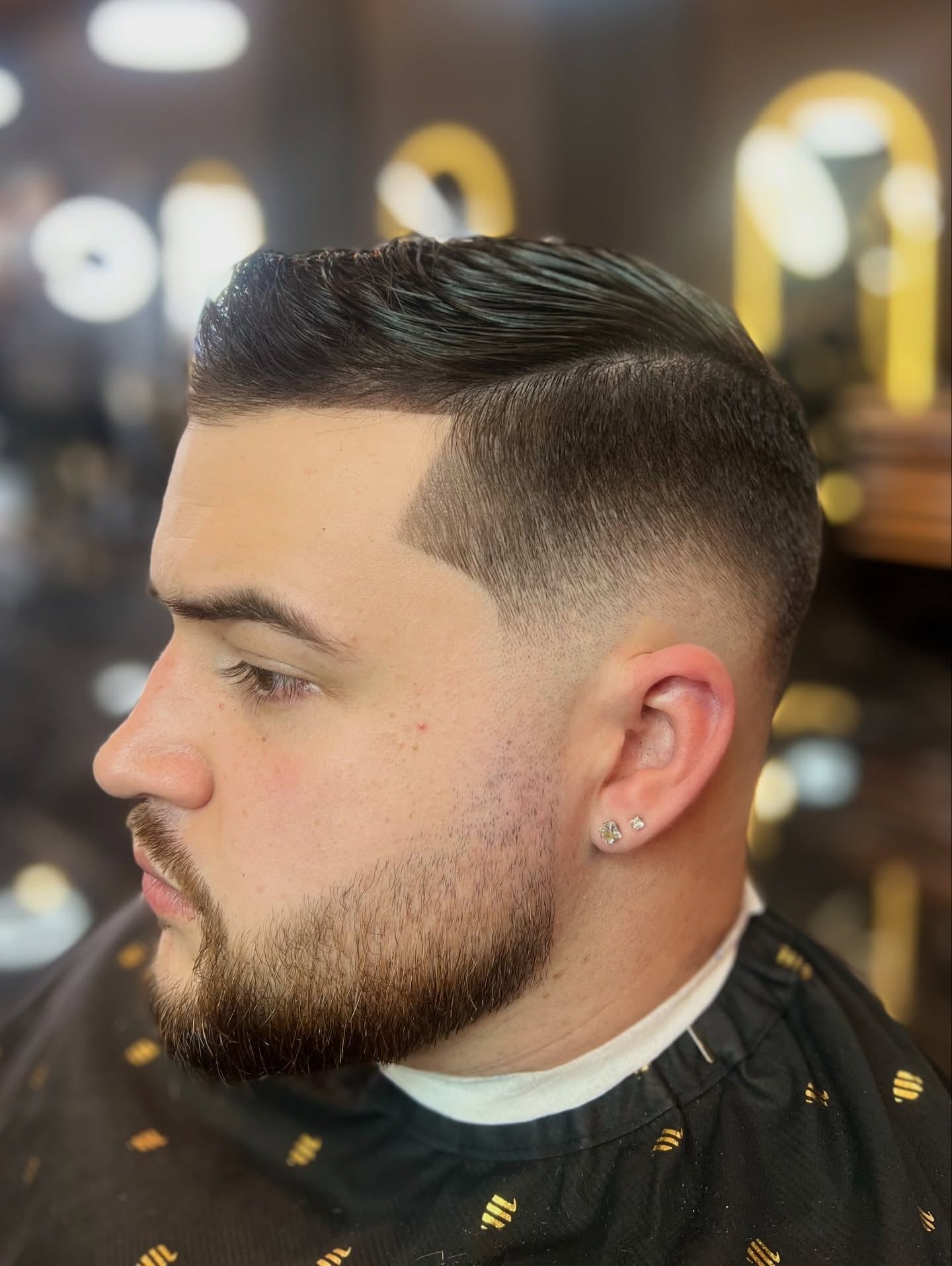 A client with a combed side part, a mid fade and a lined-up beard